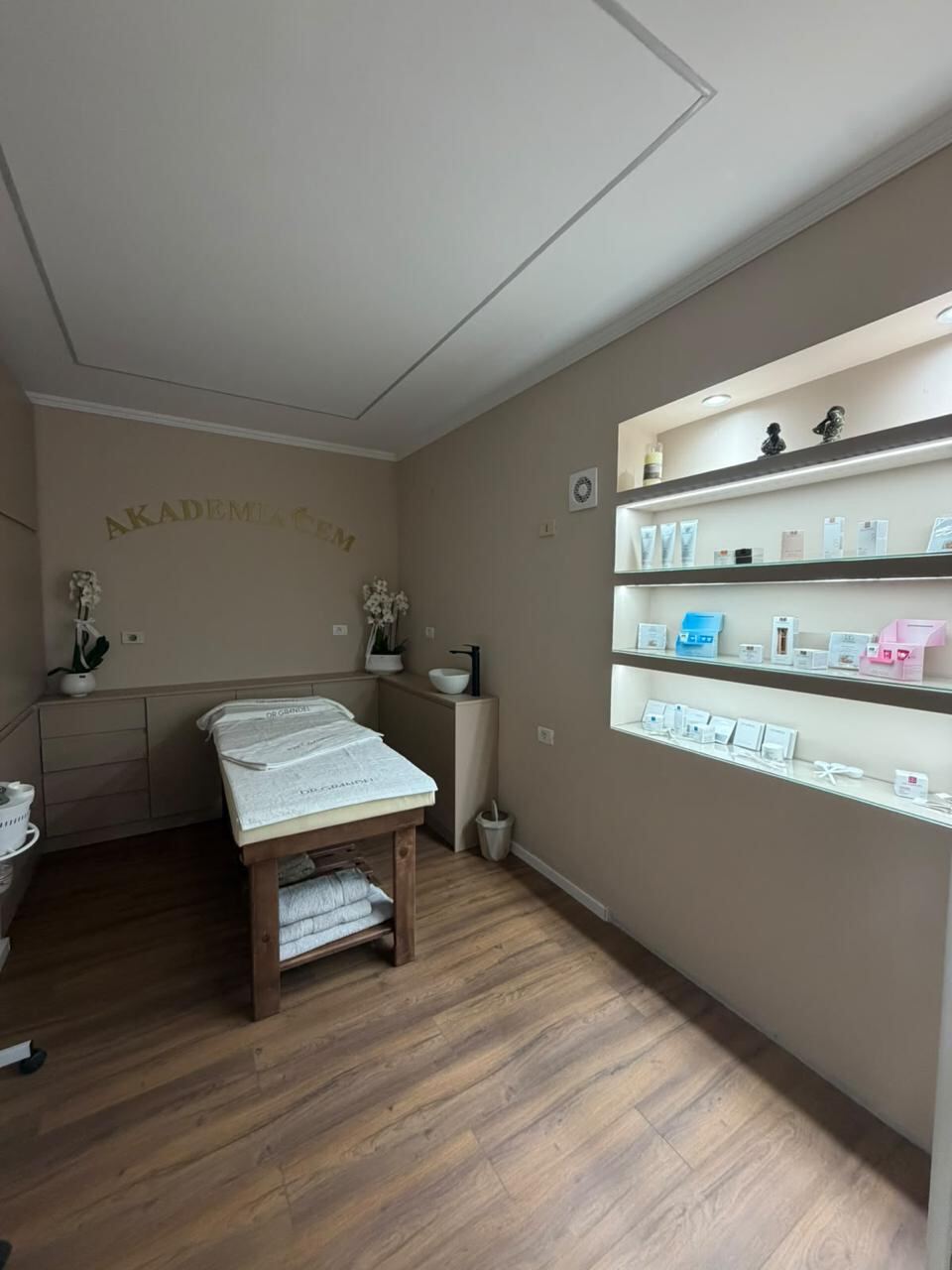 A private treatment cabin with one bed, a wash basin and a lit shelf of skincare products.